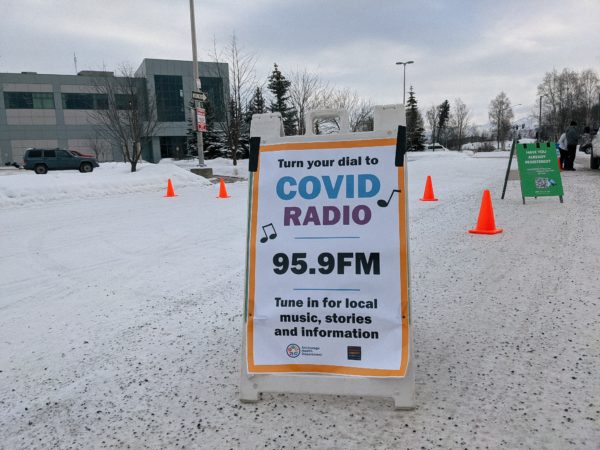 A sign in a snowy parking lot reads "COVID Radio 95.9 FM."