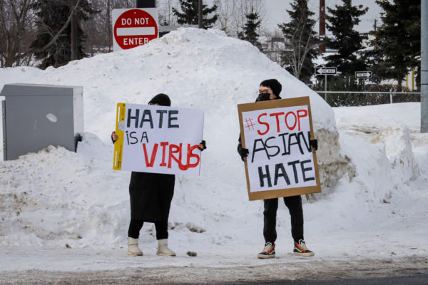 Two people hold signs that say "hate is a virus" and "stop Asian hate" on a street corner