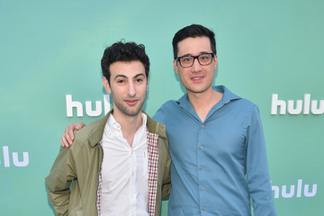 Two men face the camera, one with his arm on the other's shoulder, in front of a background that says "Hulu"