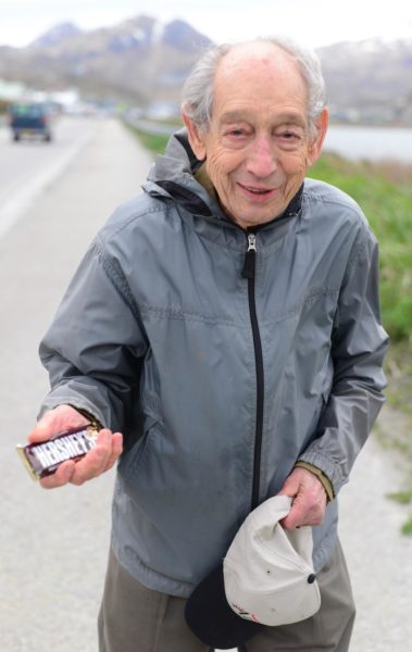An old white man in a gray wind breaker holds a hershey bar