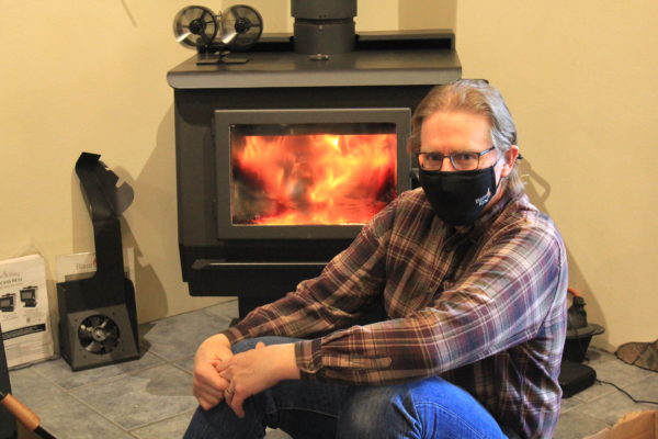 man sits in front of roaring woodstove