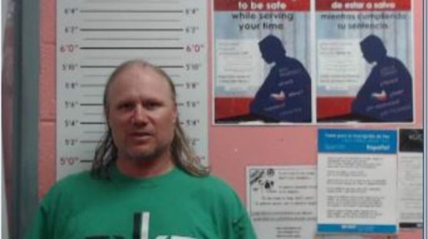 A man with a green T shirt faces the camera for a mugshot in front of lines showing his height.