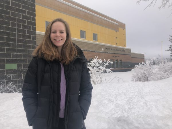 A girl stands for a photo in winter in front of her high school building