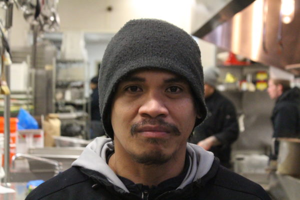 A filipino man wearing a beanie in front of a kitchen