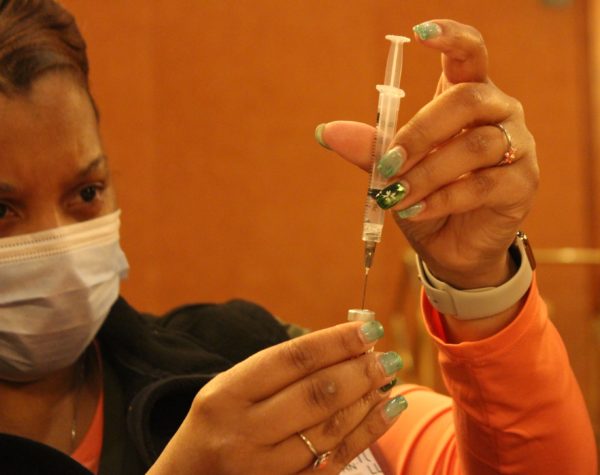 A nurse draws vaccine from a vial with a syringe