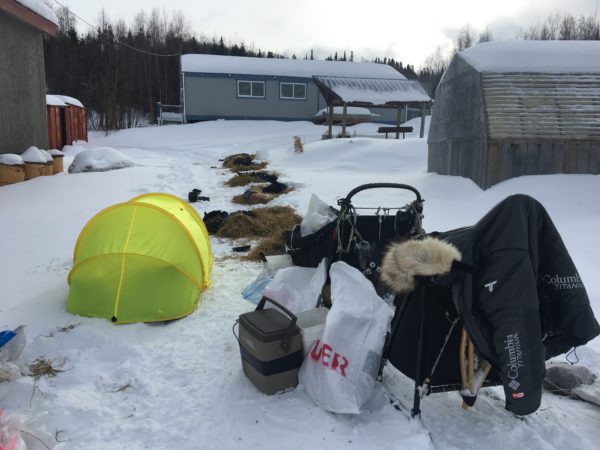 A yellow tent next to a sled in a snowy village.