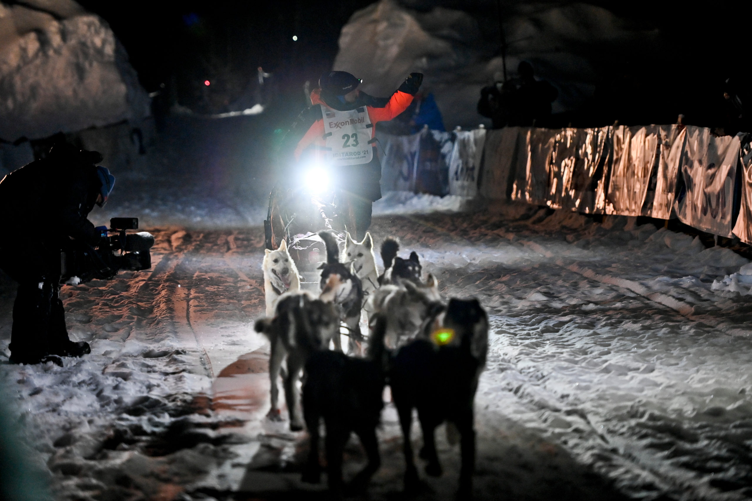 A dog musher and sled dogs race into a snowy finish line.