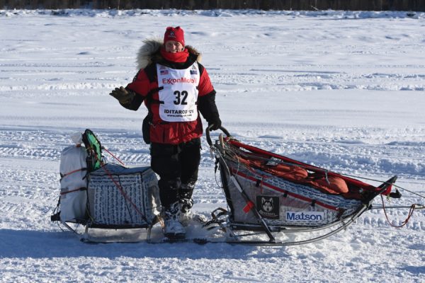 A musher waives to the crowd.