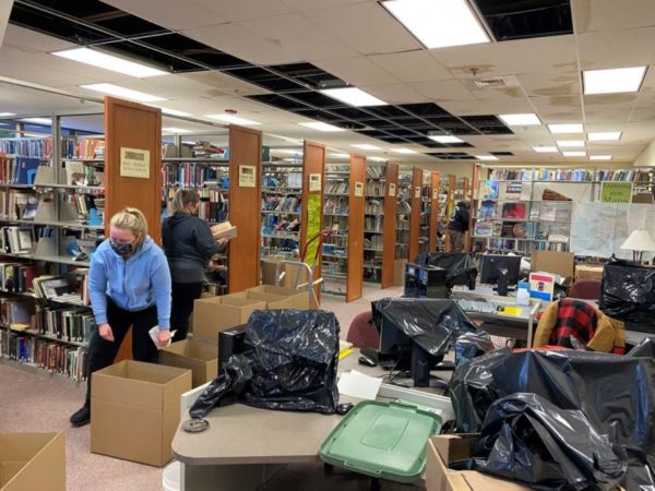 Wmen pack up books into boxes in front of rows of shelves of books