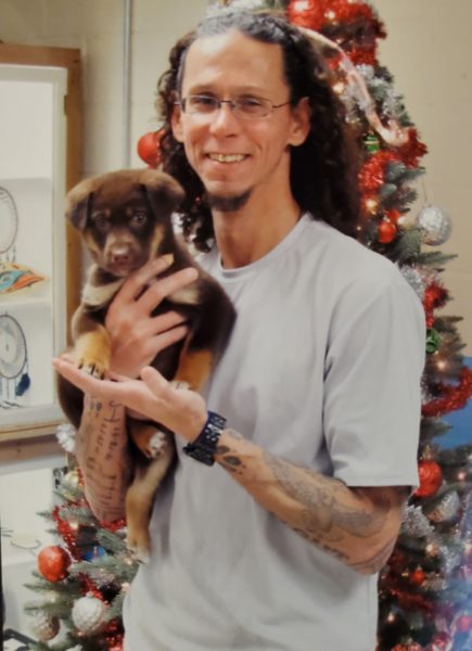 A man holds a dog in front of a christmas tree