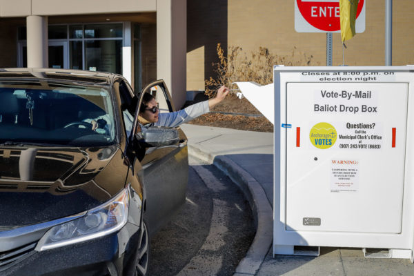a person reaches out their car door to drop off a ballot in a secure ballot box.