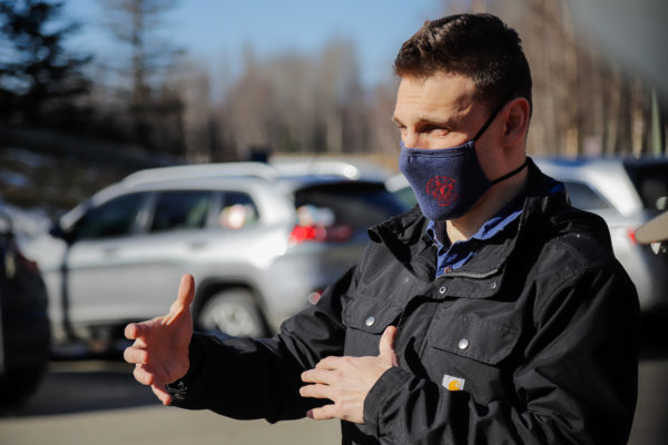 a person with a mask on speaks in a parking lot