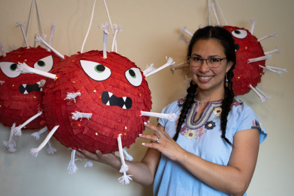 a woman smiling and standing between several COVID-19 piñatas