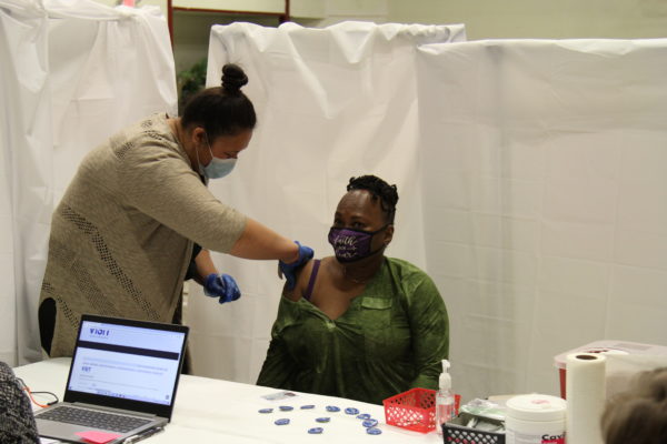 A black woman get vaccinated in her arm by a Hawaiian nurse