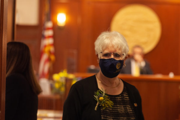A white woman with white hair wearing a mask walks in a ood panelled room