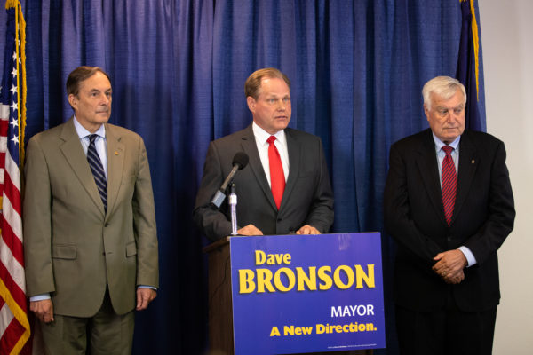 mayor elect speaks at a podium with two men next to him