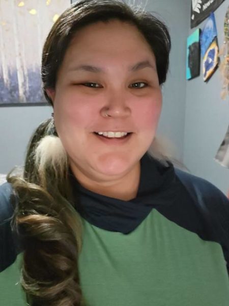A woman in a green and navy blue shirt smiles for a photo.