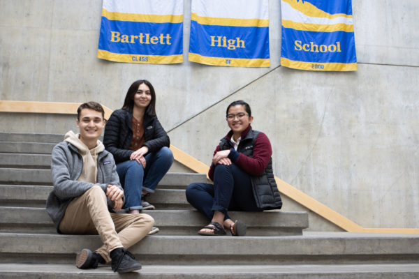 three high school students sit on steps and smile at the camera
