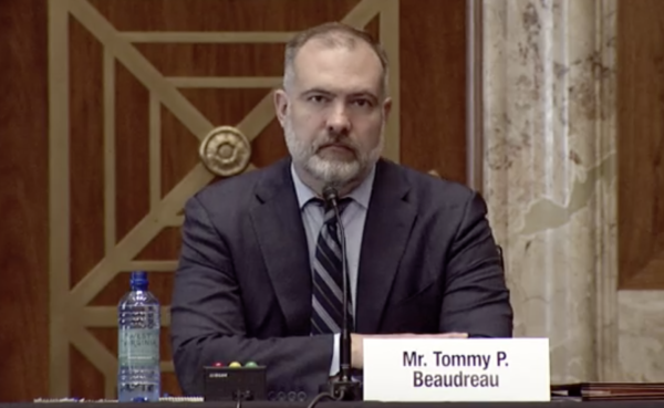 Man in suit at a microphone. name plate on desk says "Mr. Tommy P. Beaudreau"