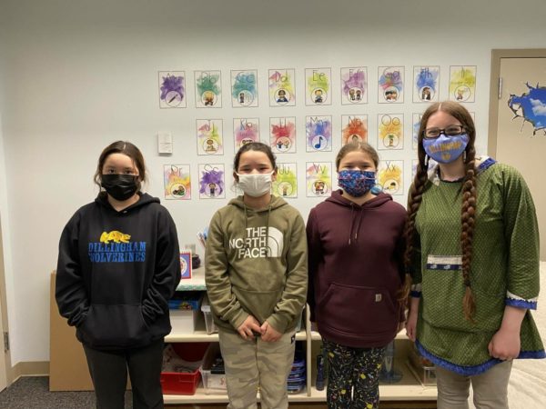 Three young girls and a female teachers stand in a line, posing or a photograph. Each one is wearing a face mask.