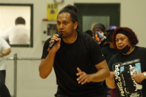 A Pacific Islander man holds a microphone and crouches 