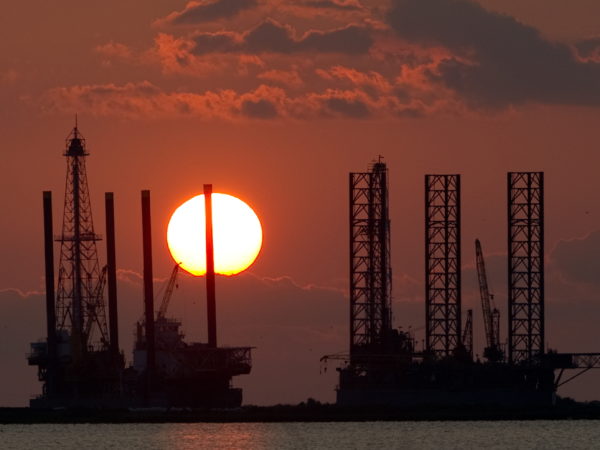 The sun sets behind big, metal oil construction platforms.