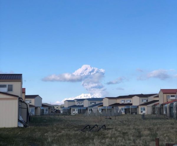 A smoke plume rises behind a subdivision of beige homes.