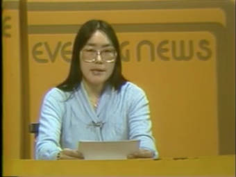 An Alaska Native woman with glasses reads from a paper at a desk