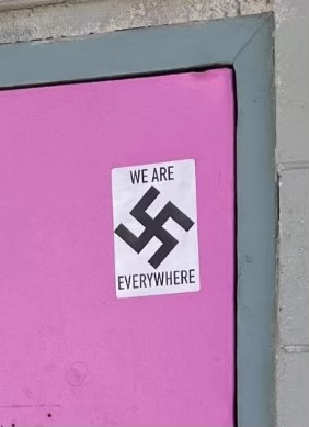 A swastika sticker in the top corner of a pink door