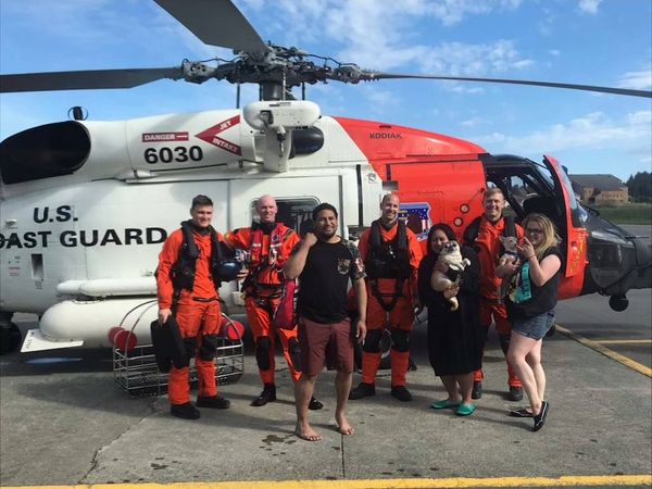 A crew of people pose in front of a coast guard helicopter