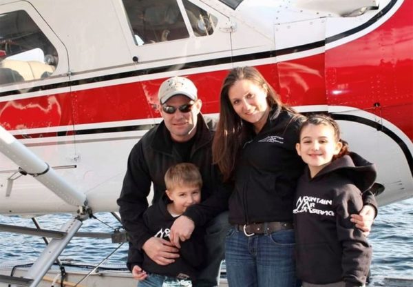 A mother, father, and two young kids pose in front of a red float plane