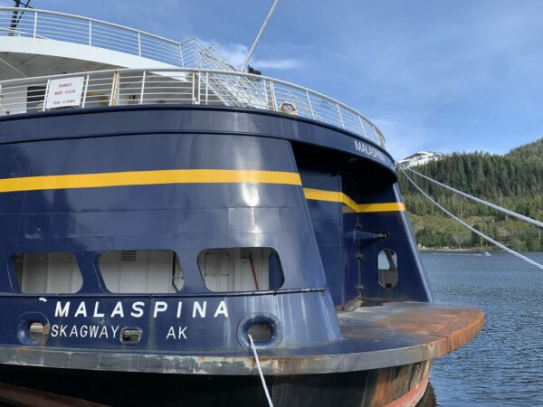 The stern of a blue boat with a yellow stripe and the name "Malaspina" on it