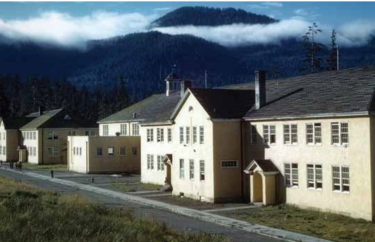 A white building with a black roof in front of some steamy mountains