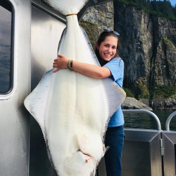 A woman hugs a giant halibut.