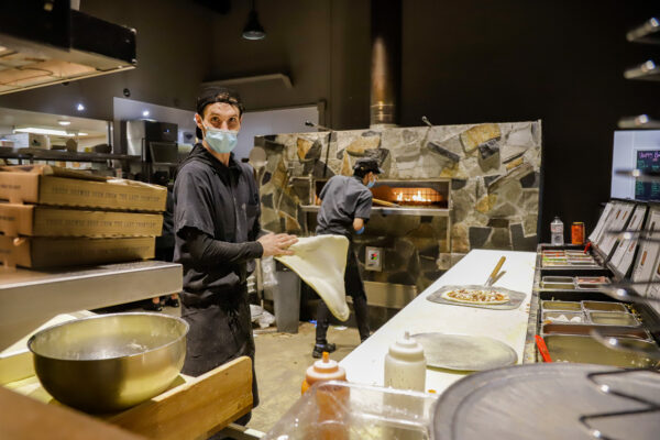 two people preparing pizzas in front of a pizza oven in a restaurant