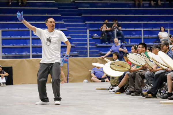 a person dances while others drum on an arena floor