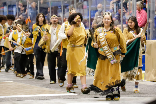 people in regalia drum and dance on an arena floor