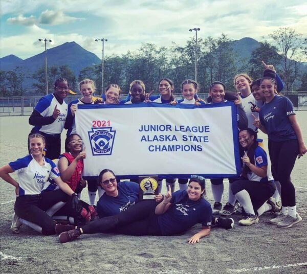 A group of girls and women stand around a sign that says Junior League Alaska State Champions.