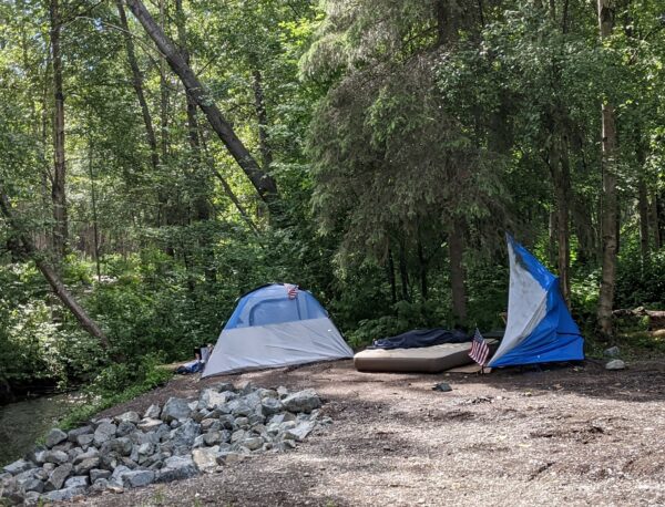 A tent on a dirt trail next to a creek 