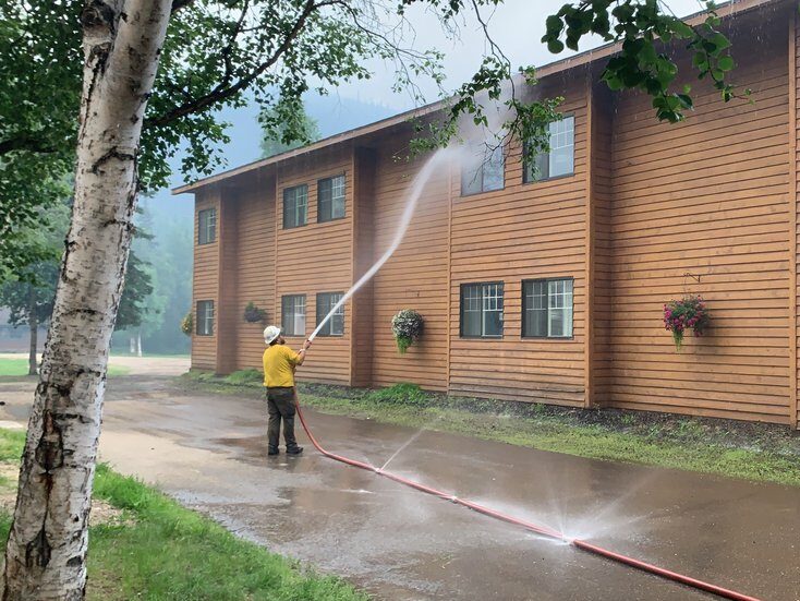 A firefighter sprays a tan buildings with a hose