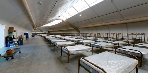 Dozens of cots in three rows span from the foreground into the distance.