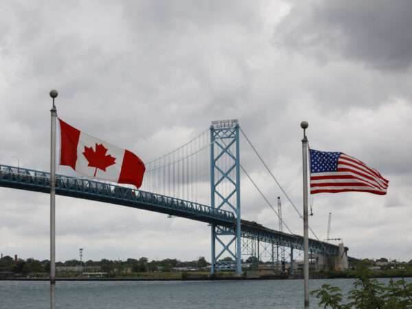 A Canadian and a U.S. flag fly near a bridge.
