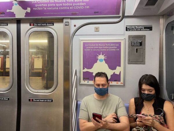 Two people on a subway looking at their cell phones wearing masks