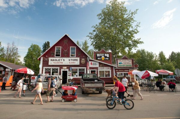 A street view of people walking and biking in front of a red general store.