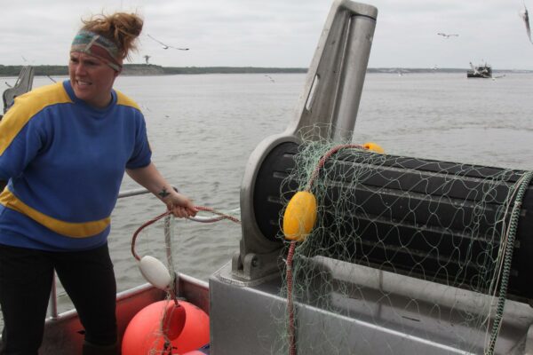 A woman pulls a net out on the deck of a boat.