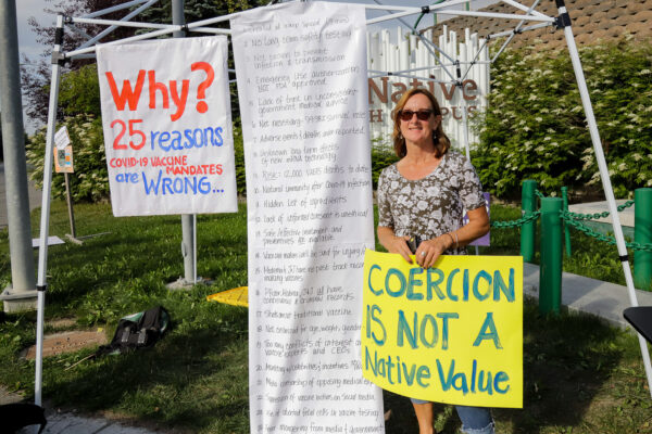 A white woman in a dress holds a yellow sign that says "Coercion is not a native value" 