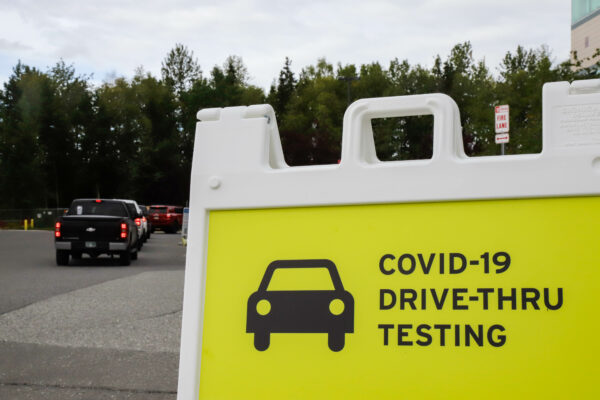 a row of cars lined up behind a sign that reads "covid-19 drive-thru testing"