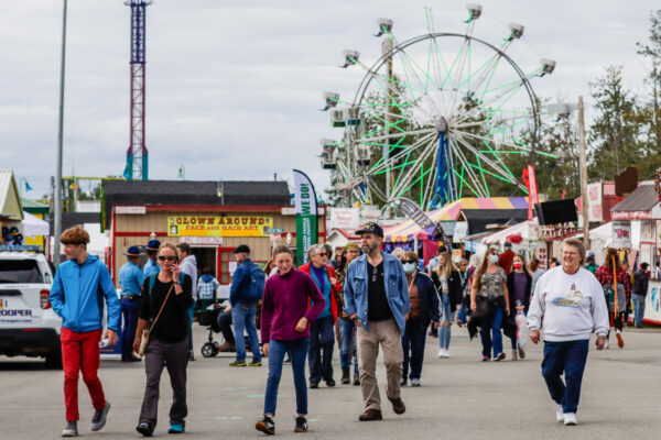 People walk through the Alaska State Fair grounds in Palmer - some masked, some not. Ferris wheel in the background