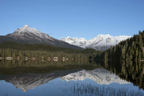 A photo of a lake with snowy mountains in the backdrop. A reflection of the mountains is also visible in the lake.