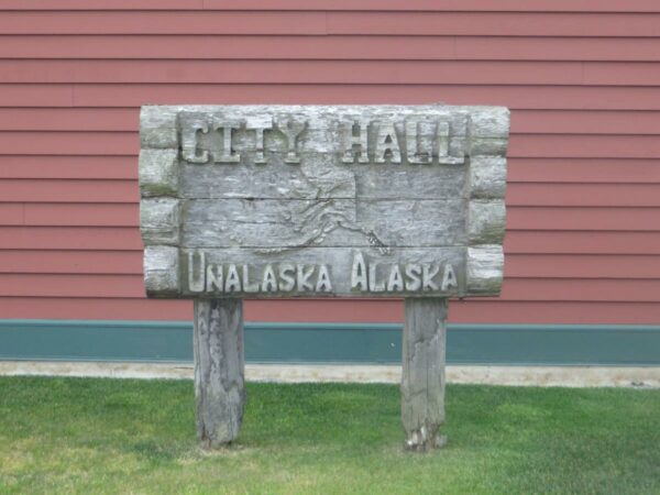 A sign reads City Hall Unalaska Alaska in front of a rust-colored building.